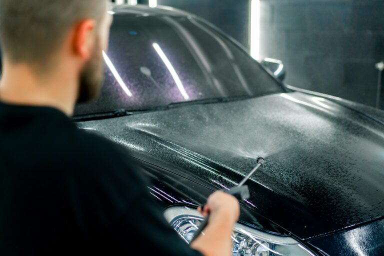 a-male-car-wash-employee-applies-car-wash-detergent-to-a-black-car-using-spray-gun-in-car-wash-box